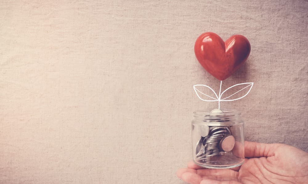 A hand holding a jar of coins and a heart balloon representing charitable giving