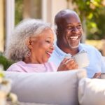 A happy older couple sits on a couch outdoors and talks about estate planning