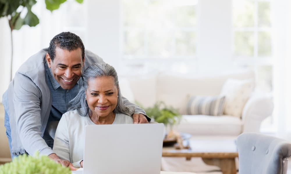An older, smiling couple looks at a laptop together to start retirement planning