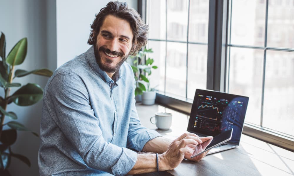 A smiling man sits at his laptop showing market performance while retirement planning
