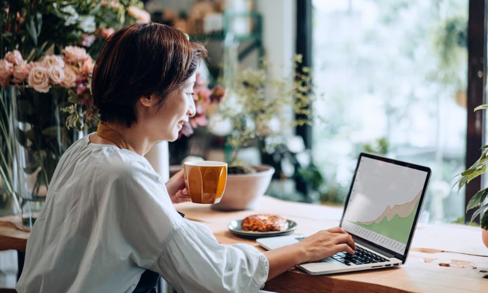 A woman drinking coffee and managing digital assets on a laptop