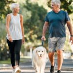 A smiling couple walks their dog while talking about wealth management
