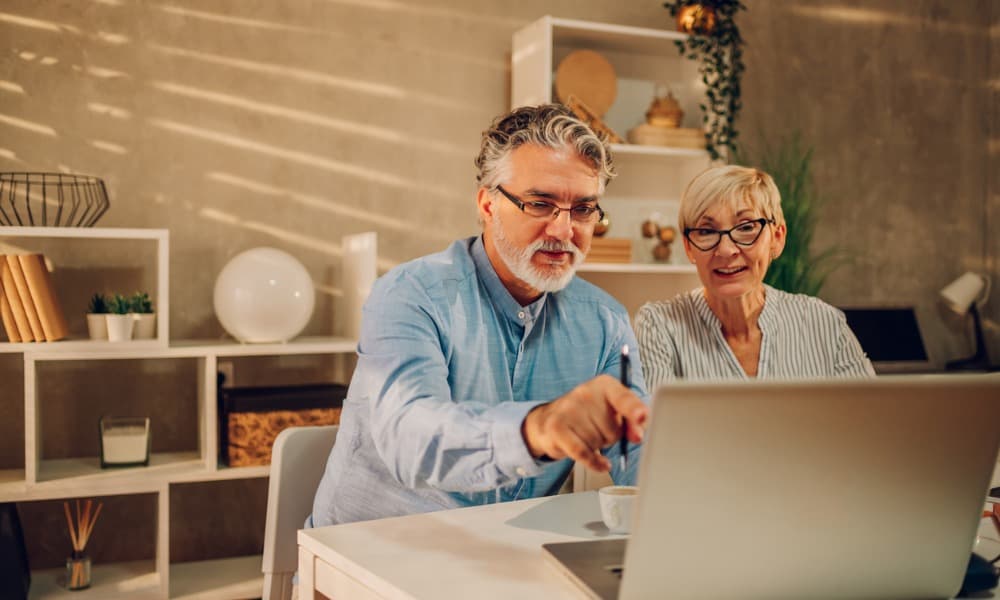 a man and woman at home looking at a laptop together and discussing retirement contributions