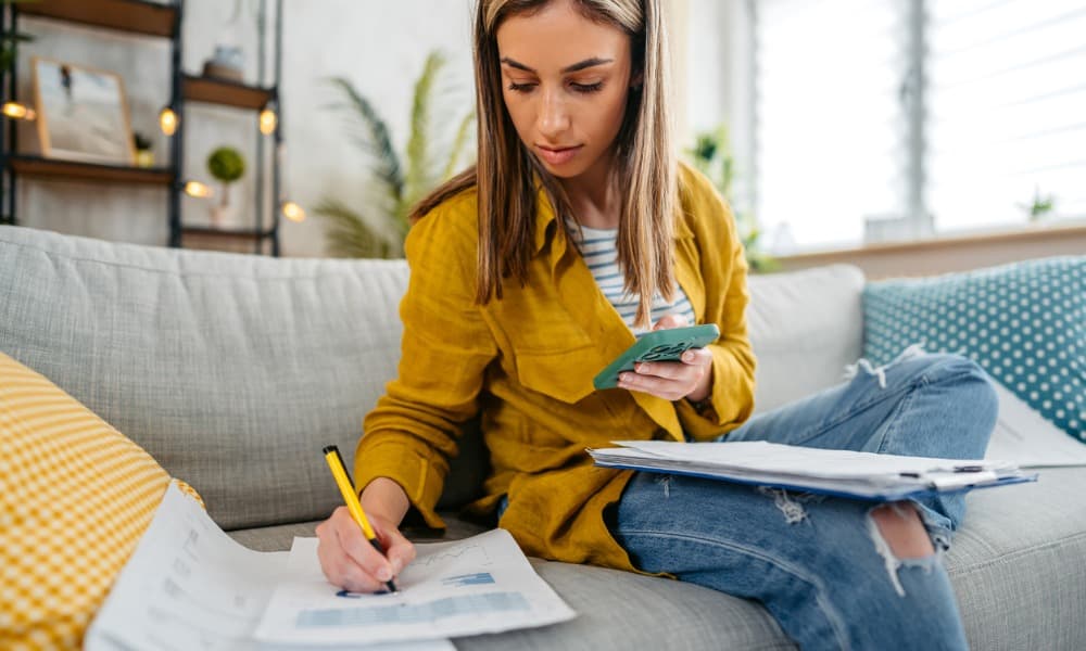 a woman doing her taxes on a couch with a calculator and wealth management paperwork