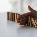 Hand stopping wooden blocks from falling representing risk management