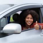 woman giving a thumbs-up in a vehicle after picking auto insurance