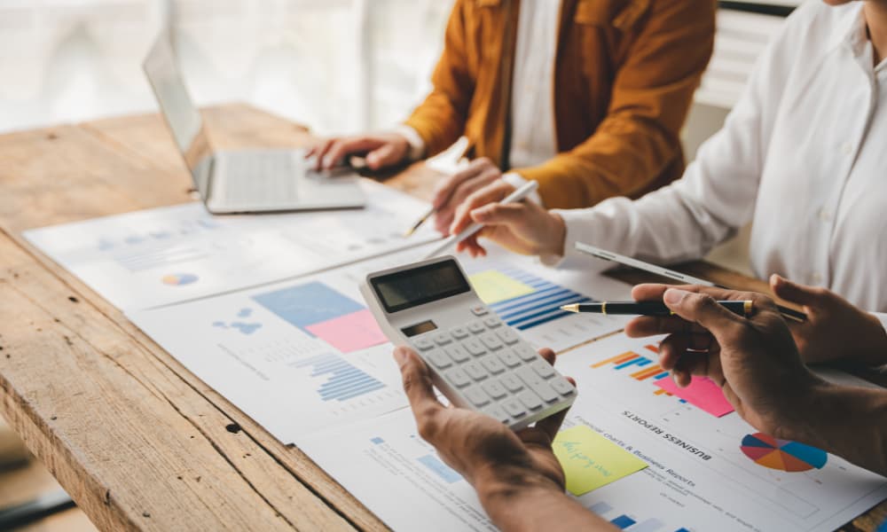 A financial advisor sitting at a desk with their client, using notebooks and calculators to work on cash flow planning with them.