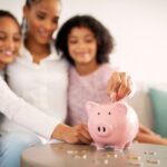 A woman and her two daughters putting coins into a piggy bank, symbolizing college savings.