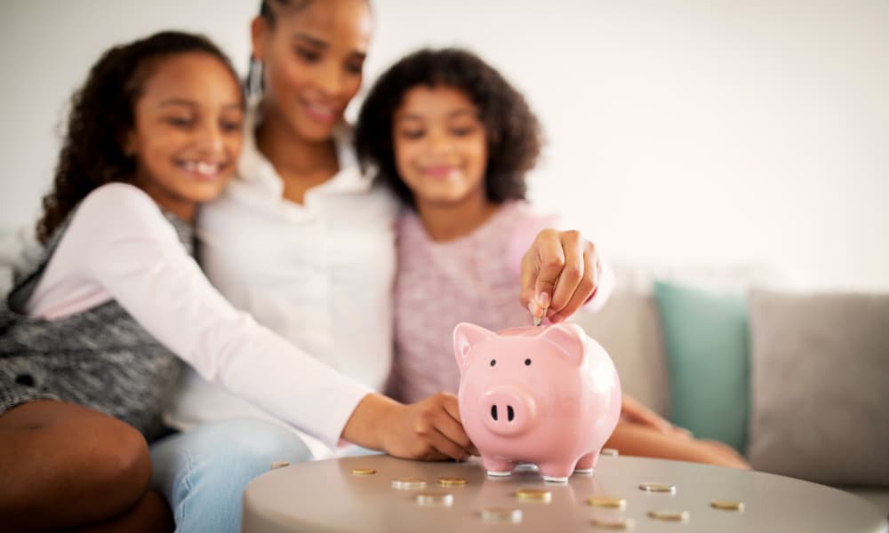 A woman and her two daughters putting coins into a piggy bank, symbolizing college savings.