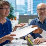 An elderly couple consults a financial advisor at a desk about making changes to their Medicare coverage.