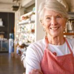 A business owner nearing retirement poses for a picture inside their retail business.