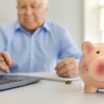 Senior man reviewing retirement finances on a laptop with a piggy bank symbolizing savings and cash flow planning.