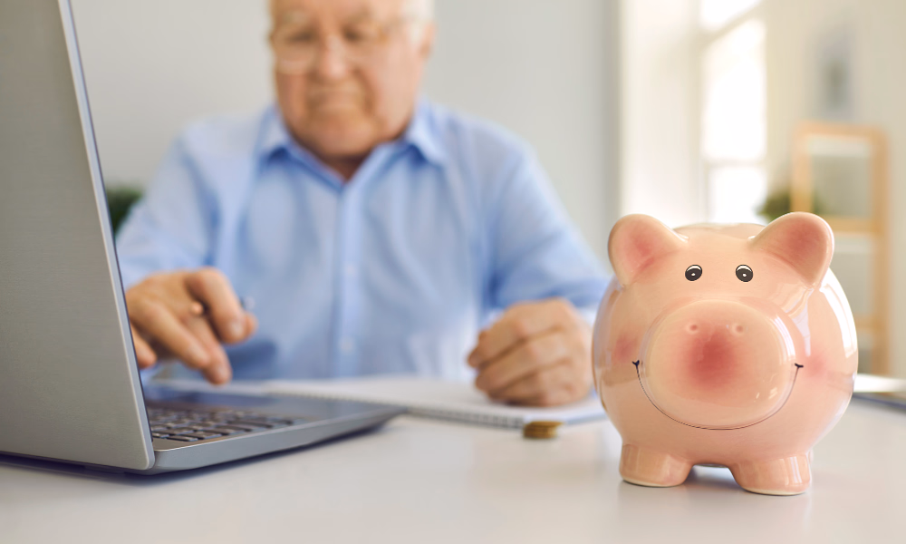 Senior man reviewing retirement finances on a laptop with a piggy bank symbolizing savings and cash flow planning.