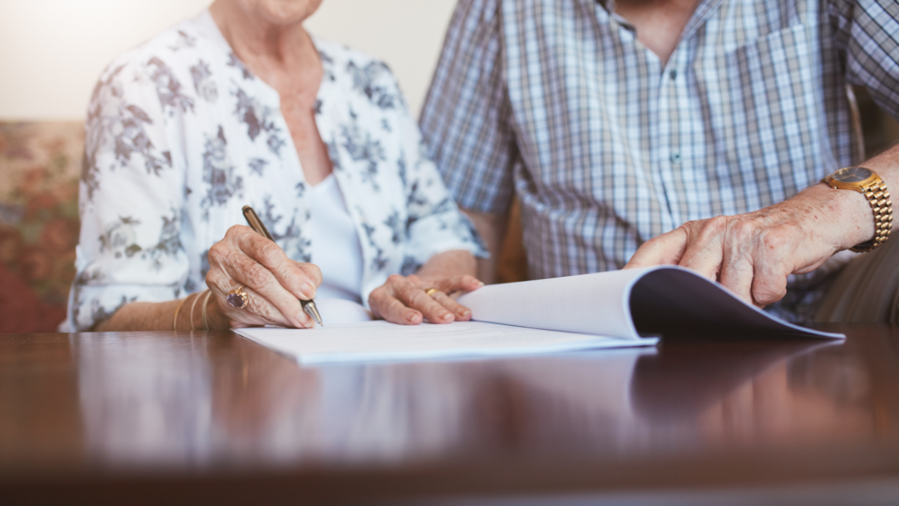 Elderly couple signing estate planning documents illustrating the importance of Will vs Trust decisions for families.