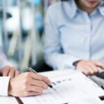 Business professionals reviewing exit planning documents and financial reports with a calculator and pen on desk.