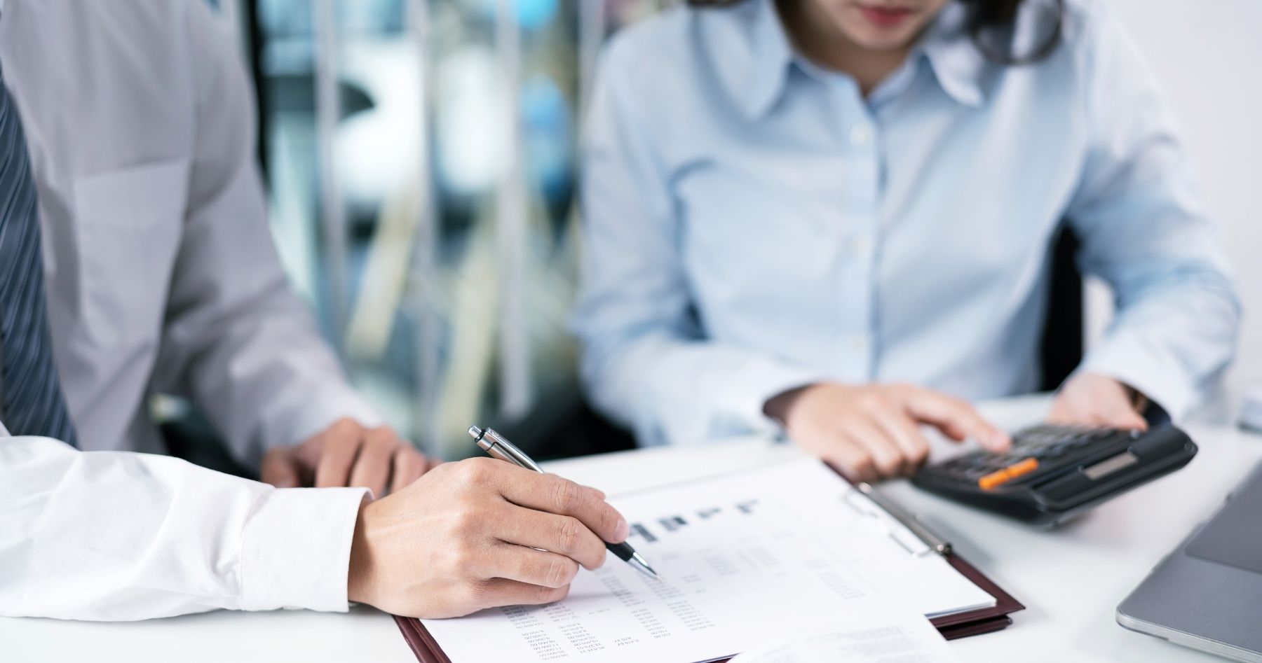 Business professionals reviewing exit planning documents and financial reports with a calculator and pen on desk.
