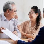 An elderly couple smiling while discussing estate planning documents with a financial advisor in an office setting.