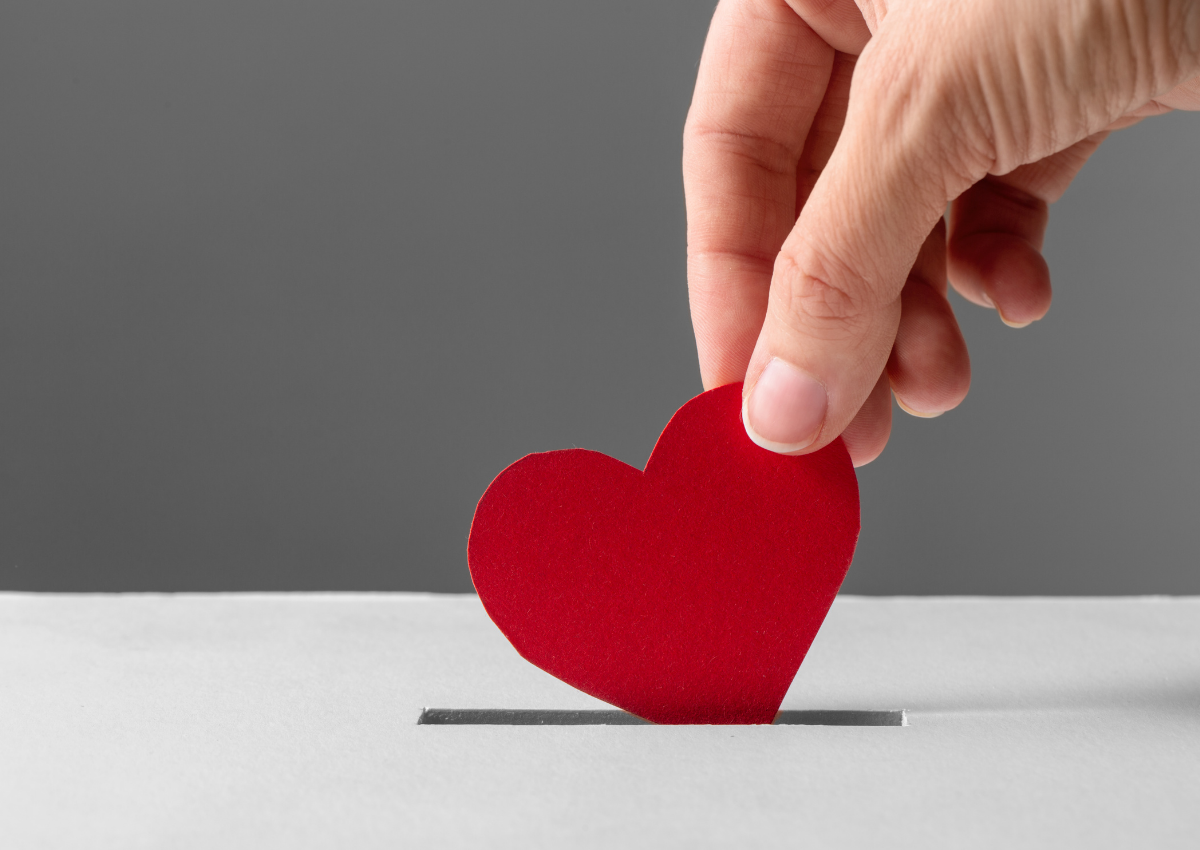Close-up of a hand placing a red paper heart into a donation box sign of charitable contributions
