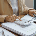 Business professional calculating finances and reviewing reports on a laptop while preparing for year-end business planning.