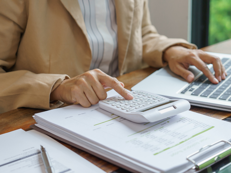 Business professional calculating finances and reviewing reports on a laptop while preparing for year-end business planning.