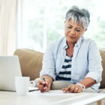 Woman reviewing retirement finances at home, completing a retirement readiness self-assessment with financial planning documents