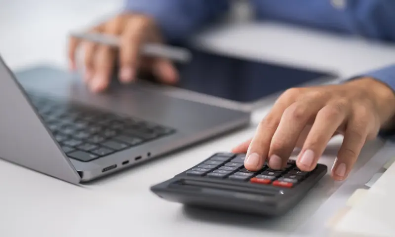 Business owner calculating quarterly tax estimates using a calculator and laptop during financial planning.