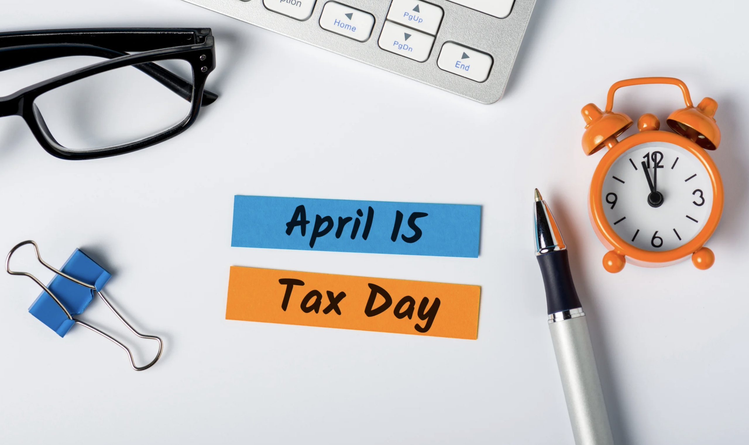 April 15 last minute tax day note with clock, pen, and office items on desk