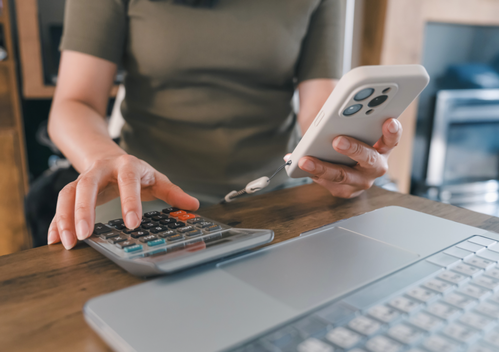 a person holding a phone and calculator in front of a laptop