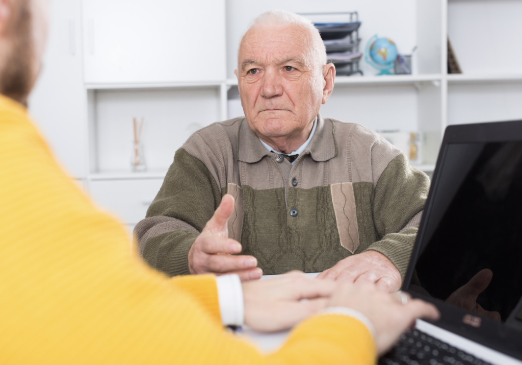 Senior man discussing financial documents with advisor during estate planning consultation and account review.