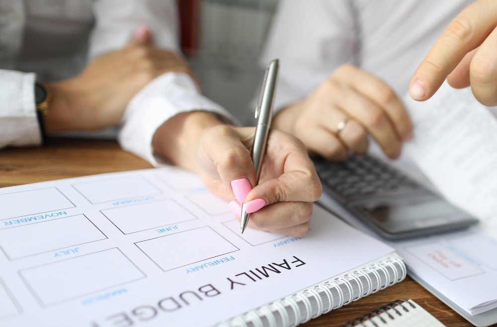 Person writing on a family budget planner with calculator nearby