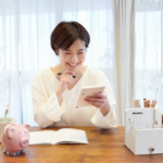 Woman smiling while calculating expenses on a tablet at a desk with a notebook