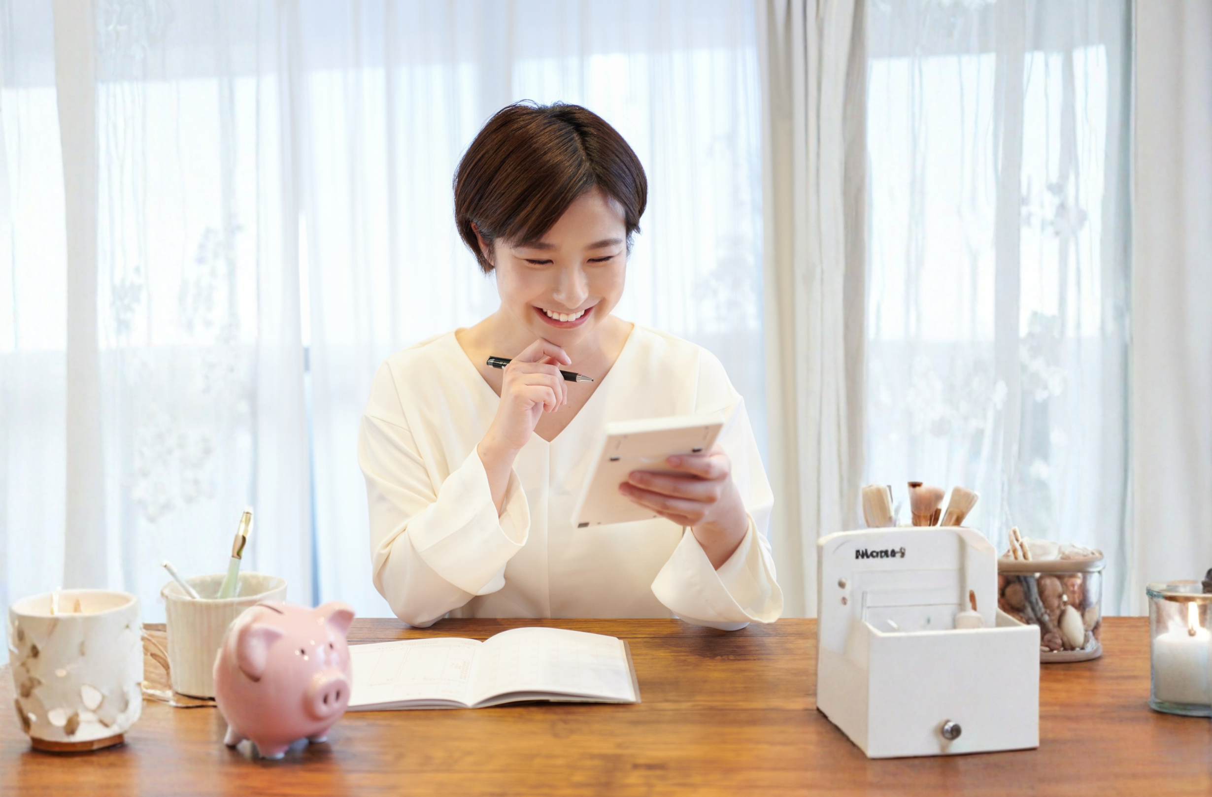 Woman smiling while calculating expenses on a tablet at a desk with a notebook