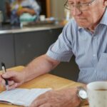 Senior man reviewing retirement finances and writing budget notes at home